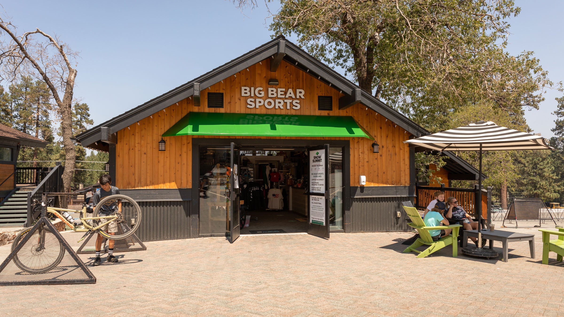 Big Bear Sports at Snow Summit during summer with a mountain biker and family sitting in lounge chairs outside the storefront