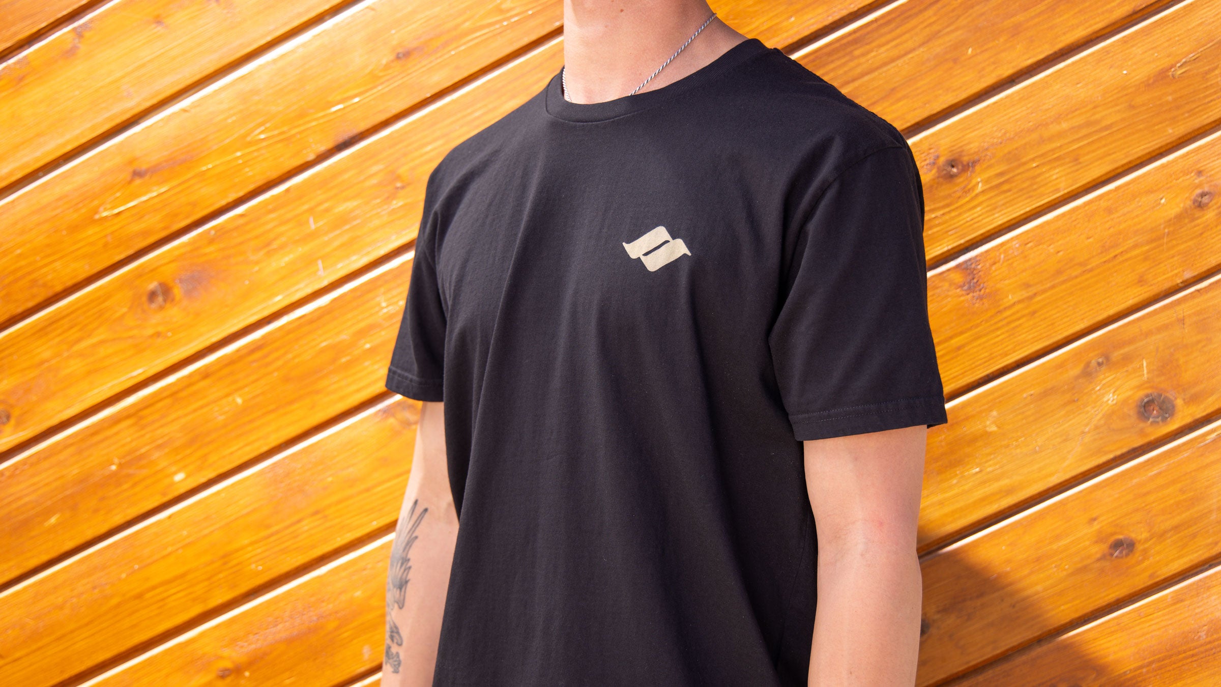 An adult wearing a black t shirt with a beige Snow Summit logo.