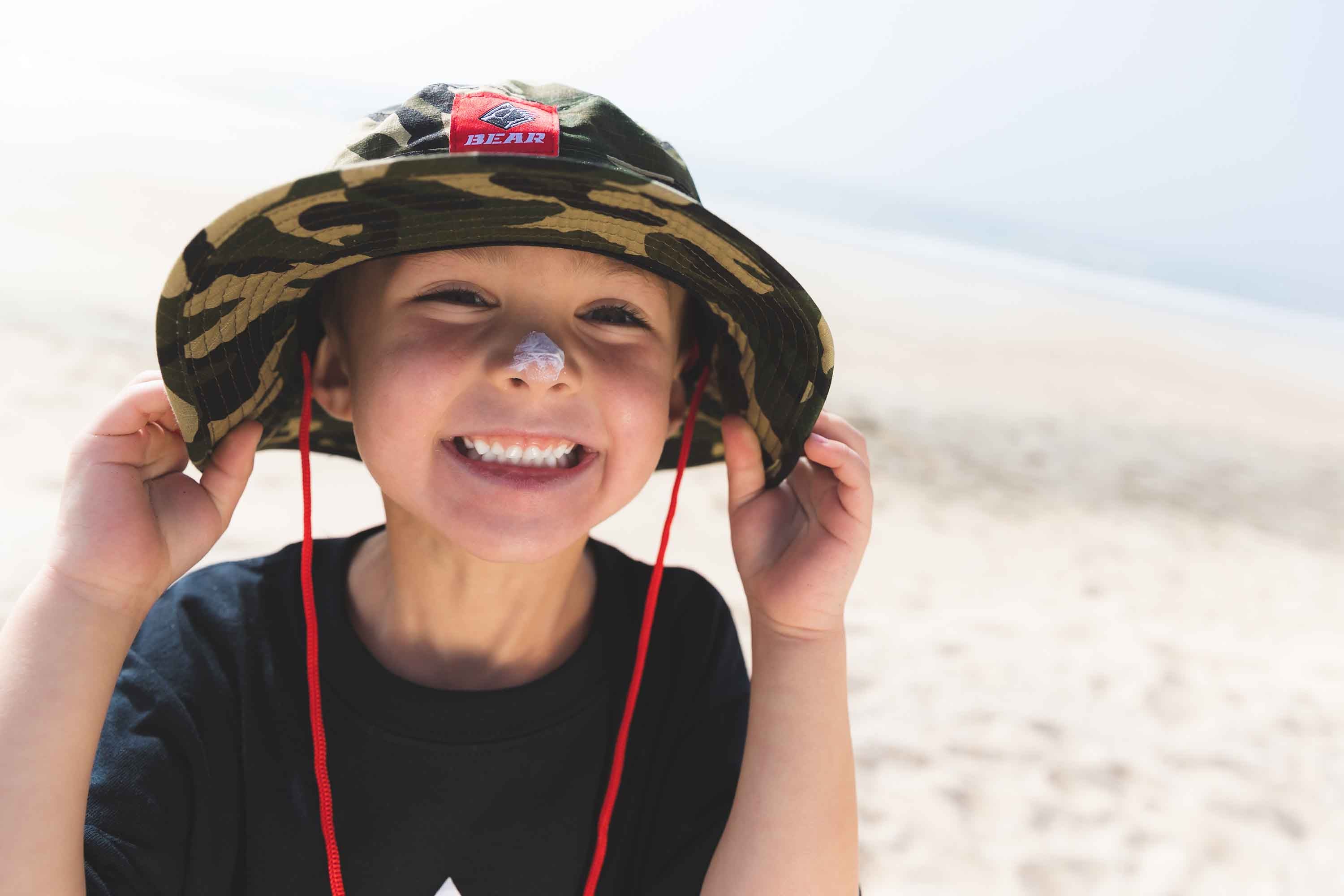 Kiddo on beach with camp bucket hat with red Bear mountain logo and drawstring