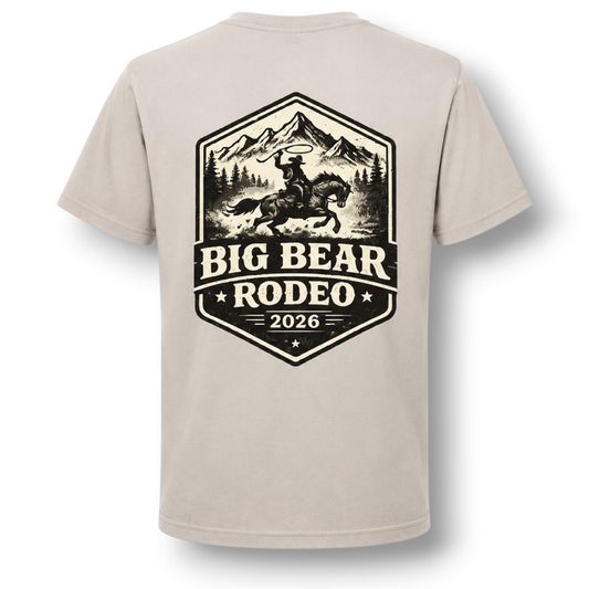 A light color crewneck t-shirt featuring a large black graphic print on the back. The graphic depicts a cowboy riding a bucking horse in front of mountains, with the text 'BIG BEAR RODEO 2026'.