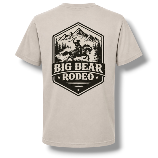 A light color crewneck t-shirt featuring a large black graphic print on the back. The graphic depicts a cowboy riding a bucking horse in front of mountains, with the text 'BIG BEAR RODEO 2026'.