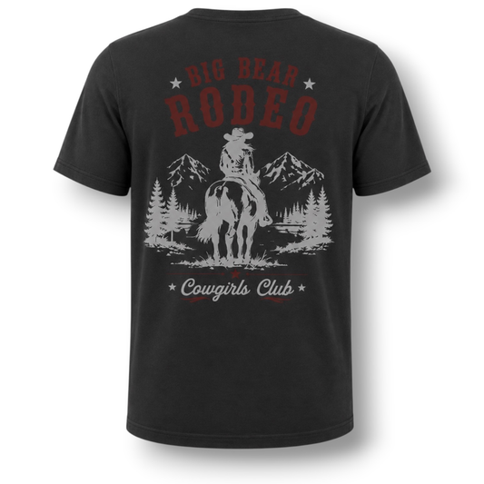 A dark gray t-shirt shown from the back, featuring a distressed graphic print of a cowgirl on a horse with mountains and pine trees, and text reading 'Big Bear Rodeo' and 'Cowgirls Club'.