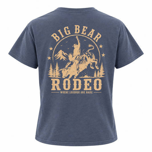 A navy blue short-sleeve t-shirt shown from the back, featuring a large tan graphic print of a cowboy riding a bucking bull with the text 'BIG BEAR RODEO' and 'WHERE LEGENDS ARE MADE'.