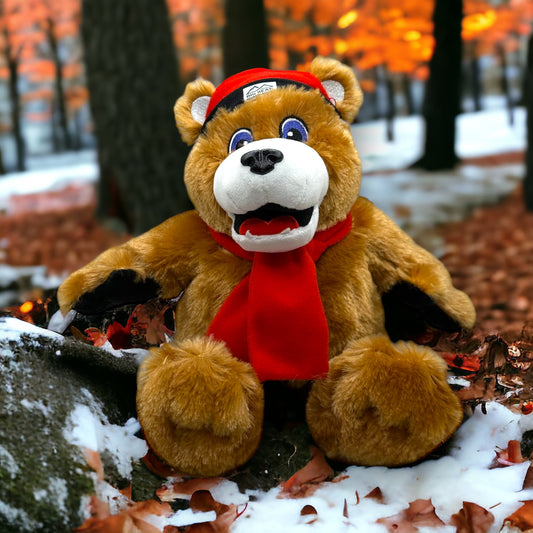 A plush brown bear toy with a red scarf and red with black brim beanie