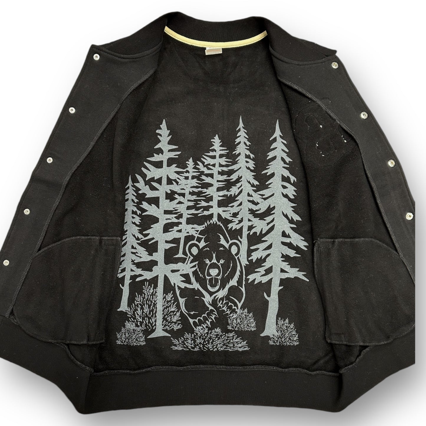 Black letterman jacket with an oversized bear and woods photo in light color on inside of jacket.