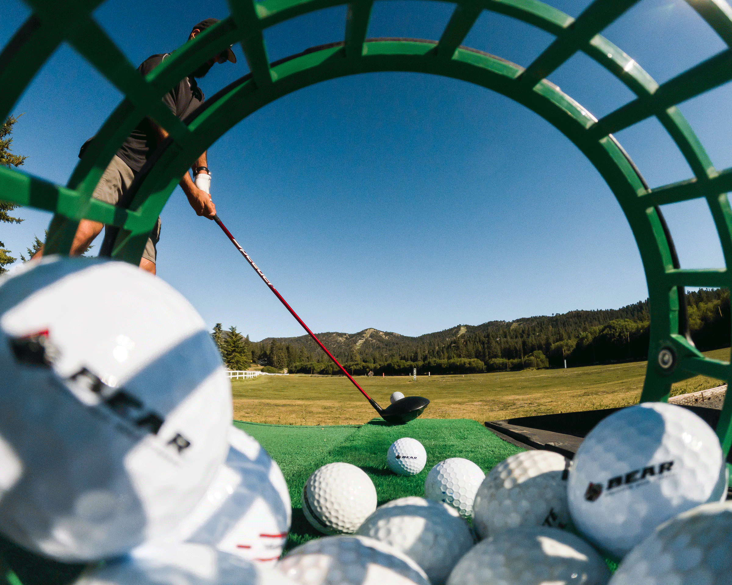 View through bucket filled with golf balls and a golfer about to hit the ball
