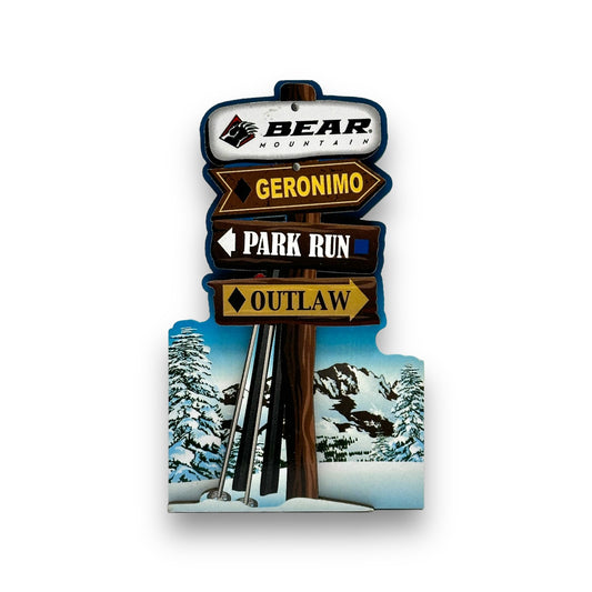 This wooden magnet features a snowy base with skis and ski poles leaning against a wooden post, showcasing the Bear Mountain logo at the top and the three main winter trails below.