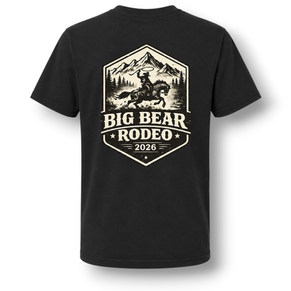 A black short-sleeve t-shirt with a large white colored graphic on the front. The graphic features a design with a cowboy riding a bucking horse in front of mountains, with the text 'BIG BEAR RODEO' and '2026' below.