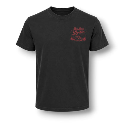 A black short-sleeve crewneck t-shirt with a small red graphic on the left chest reading 'Big Bear Rodeo' above a mountain and trees illustration, shown on a white background with a soft drop shadow.