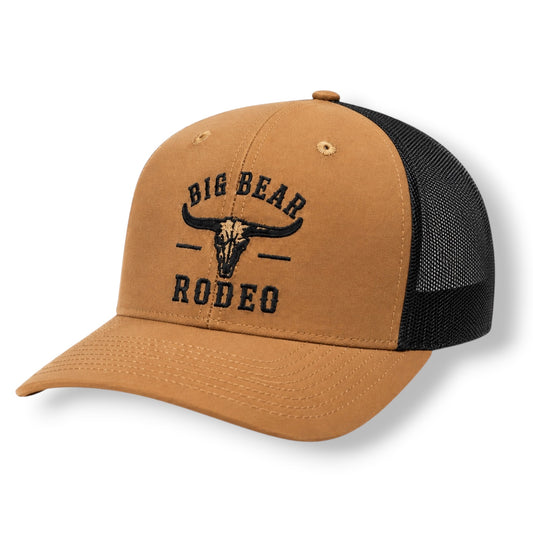 A tan orange with black mesh trucker hat with 'BIG BEAR RODEO' and a bull skull graphic embroidered on the front, shown on a white background.