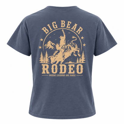 A navy blue short-sleeve t-shirt shown from the back, featuring a large tan graphic print of a cowboy riding a bucking bull with the text 'BIG BEAR RODEO' and 'WHERE LEGENDS ARE MADE'.