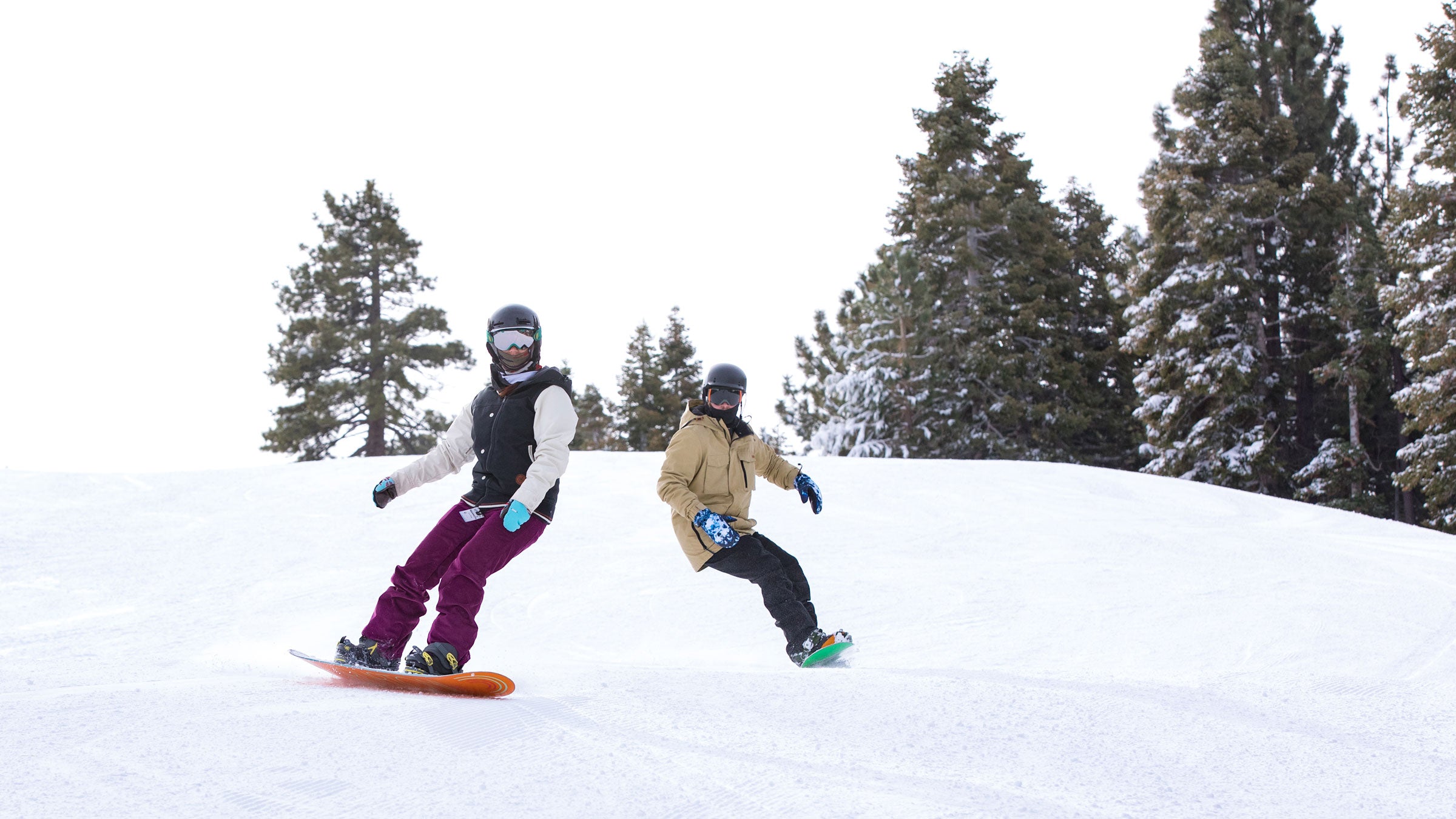 Two snowboarders carving down the slopes