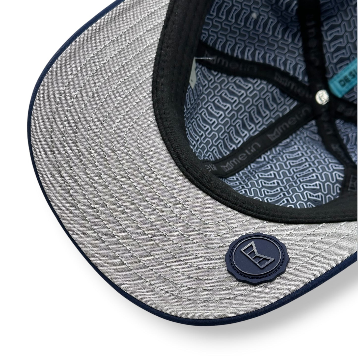 Close-up of a gray under bill of a navy cap with Melin brand logo.