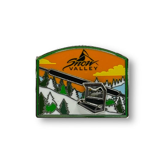 Snow Valley moving chairlift metal pin with a mountain scenery with green pine trees and a orange sky with white clouds
