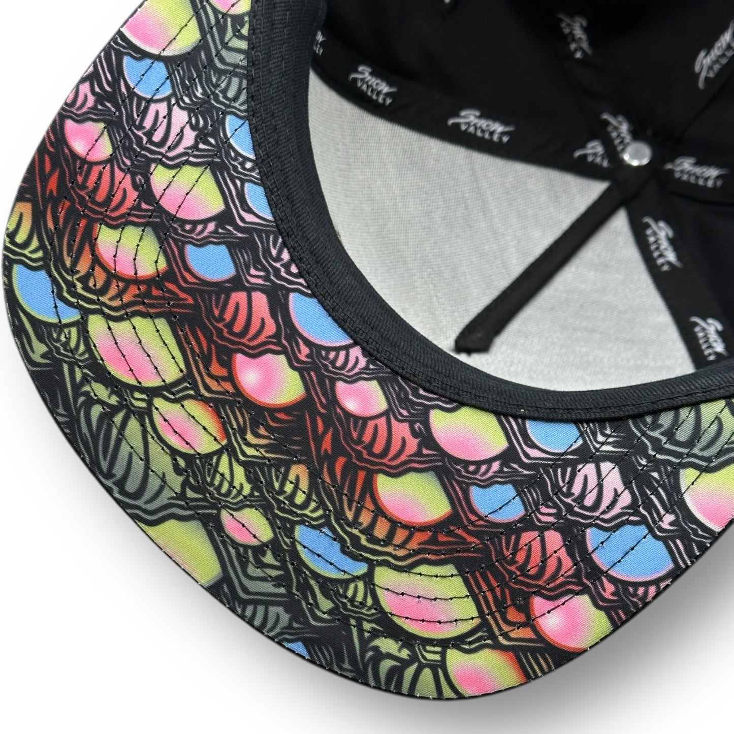 The underside of a Snow Valley hat with dark color and colorful fish scale pattern under the brim.